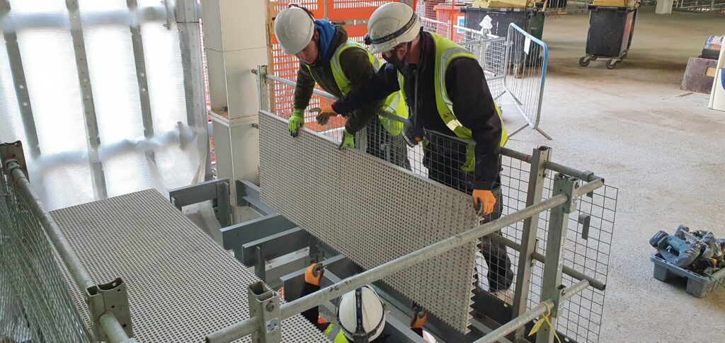 Two installers lowering a panel of GRP grating onto the the framework