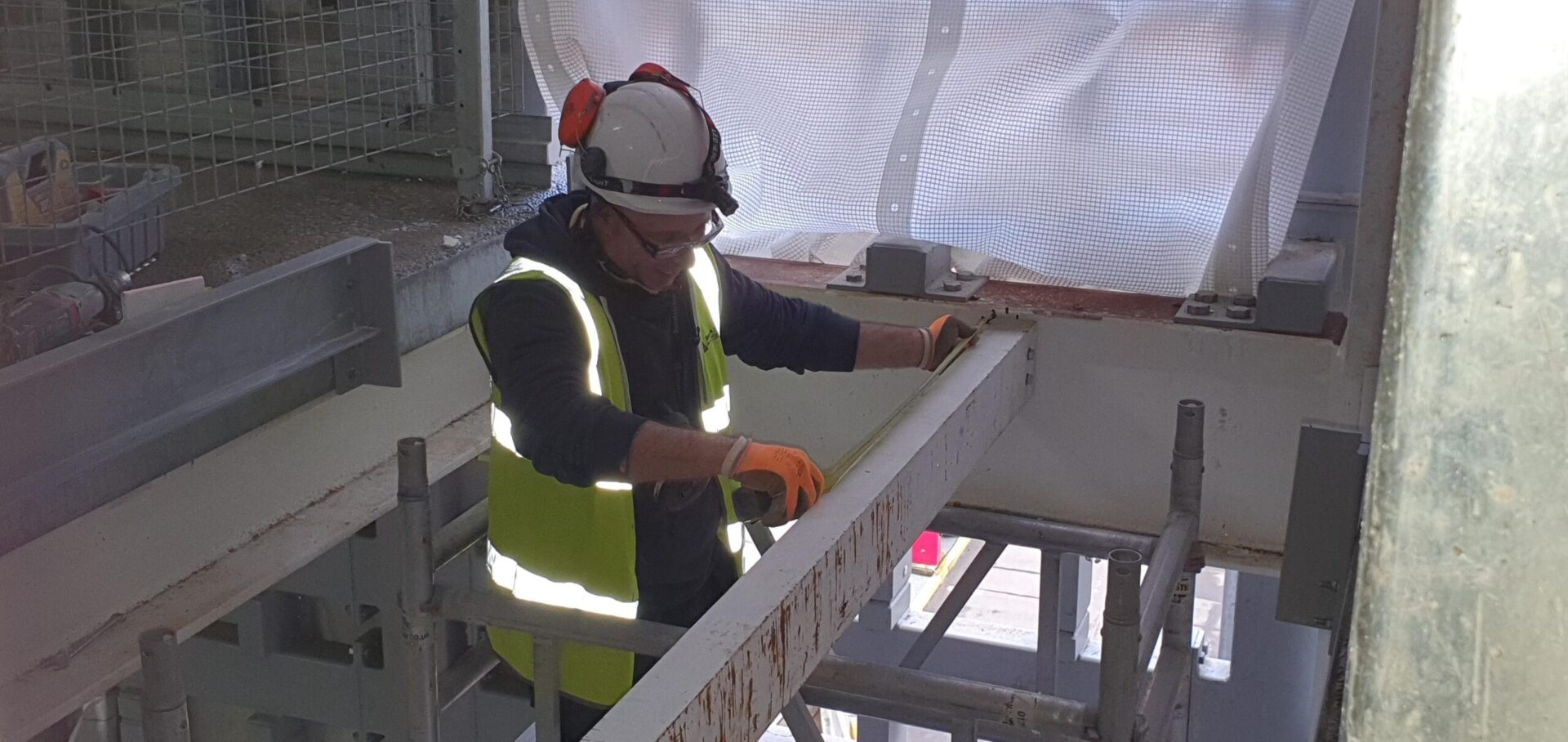 A Step on Safety installer measuring a horizontal beam in a service riser