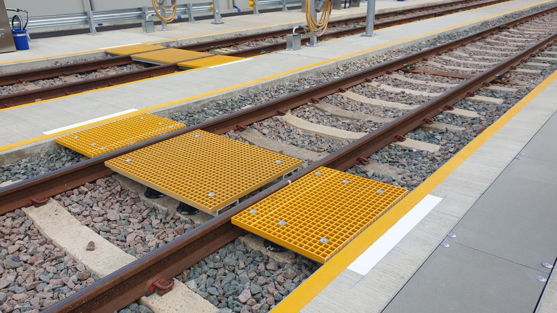 A GRP open mesh walkway comprising yellow mesh panels cut to fit between railway tracks to create a trip-free route from one side of the depot to the other