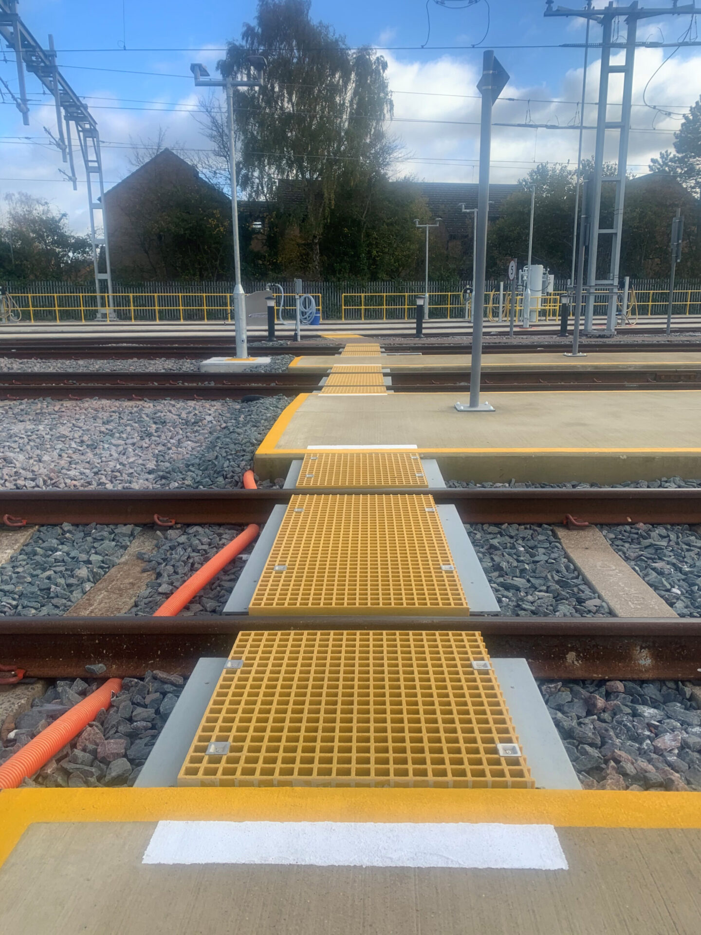 A GRP open mesh walkway comprising yellow mesh panels cut to fit between railway tracks to create a trip-free route from one side of the depot to the other