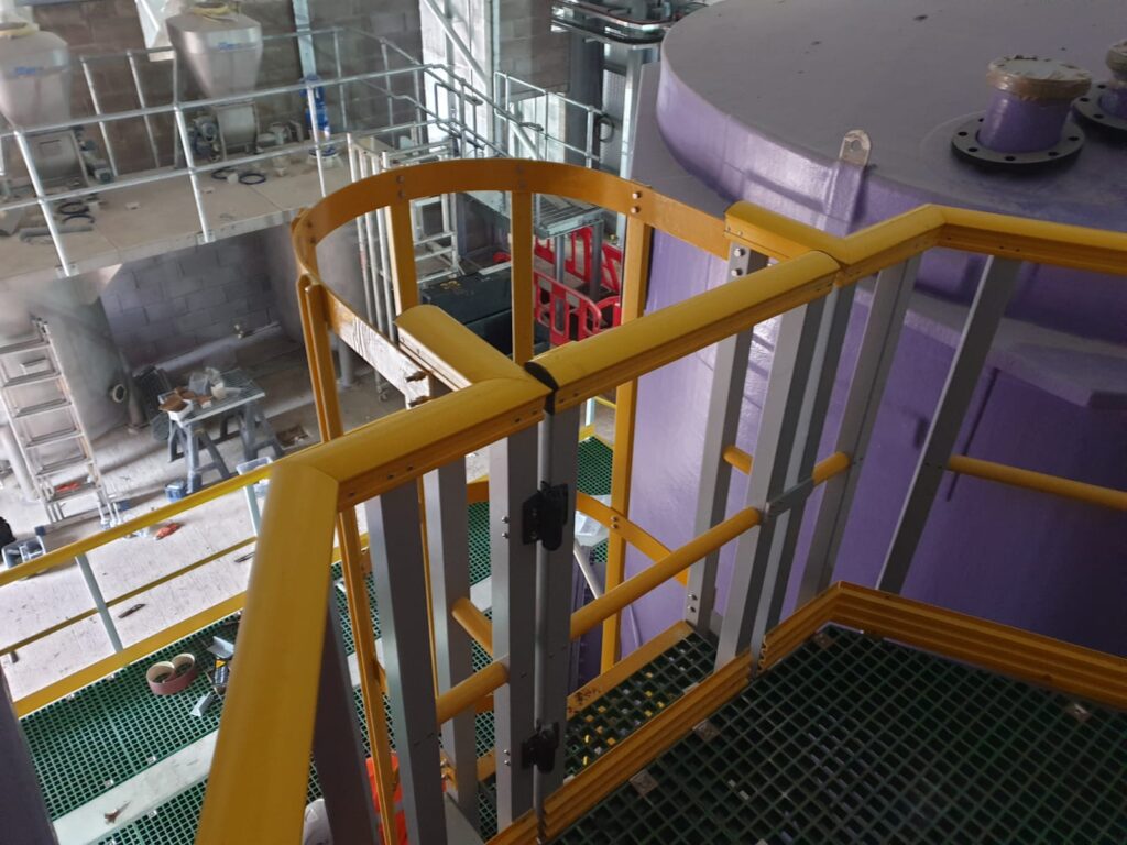 A shot taken from the top of a maintenance platform showing the self-closing gate and safety hoops at the top of the access ladder