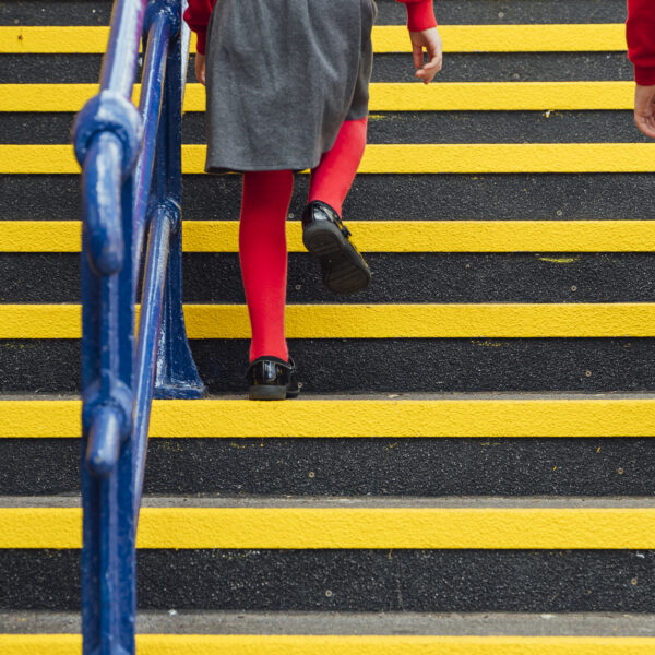 A low angle legs only view of a boy and a girl walking upstairs in a public transport station with yellow QuartzGrip Anti-Slip stair nosing on each step