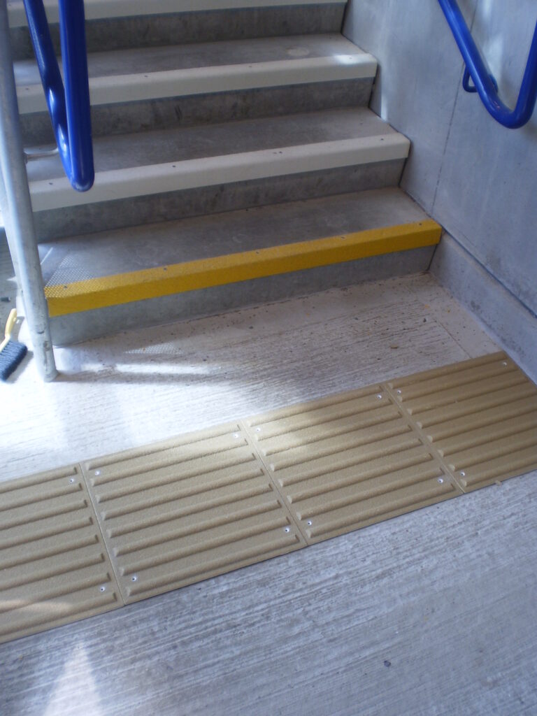 Corduroy tactile flooring at the foot of a staircase to warn those with visual impairment of the trip hazard