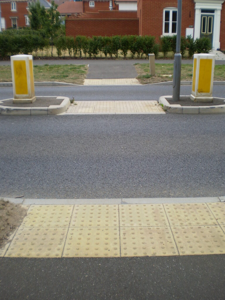 Inline blister tactile flooring at a road crossing to warn those with visual impairment of the potential hazard