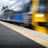 Modern train racing through railway station in Scotland with tactile flooring near the edge of the platform