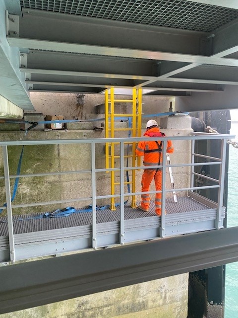 Photo shows a installer in orange hi-vis working on a yellow GRP cat ladder that provides access to the maintenance platform below the pier at the Port of Dover