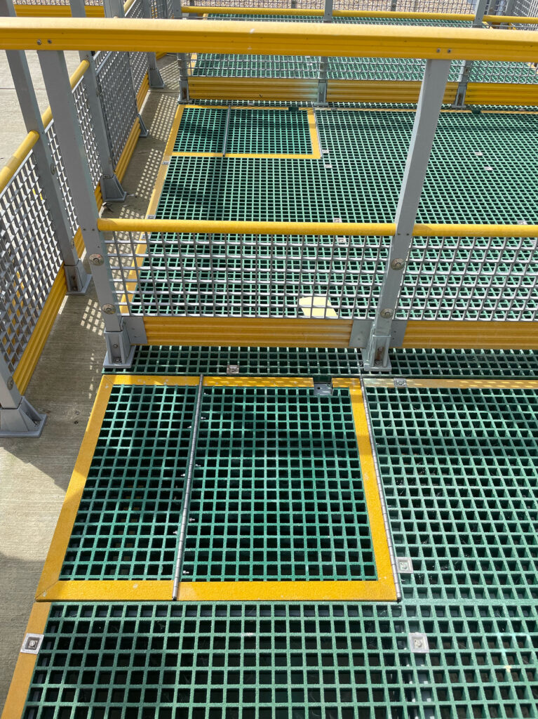 Photo shows a manhole cover set into green grating chamber cover